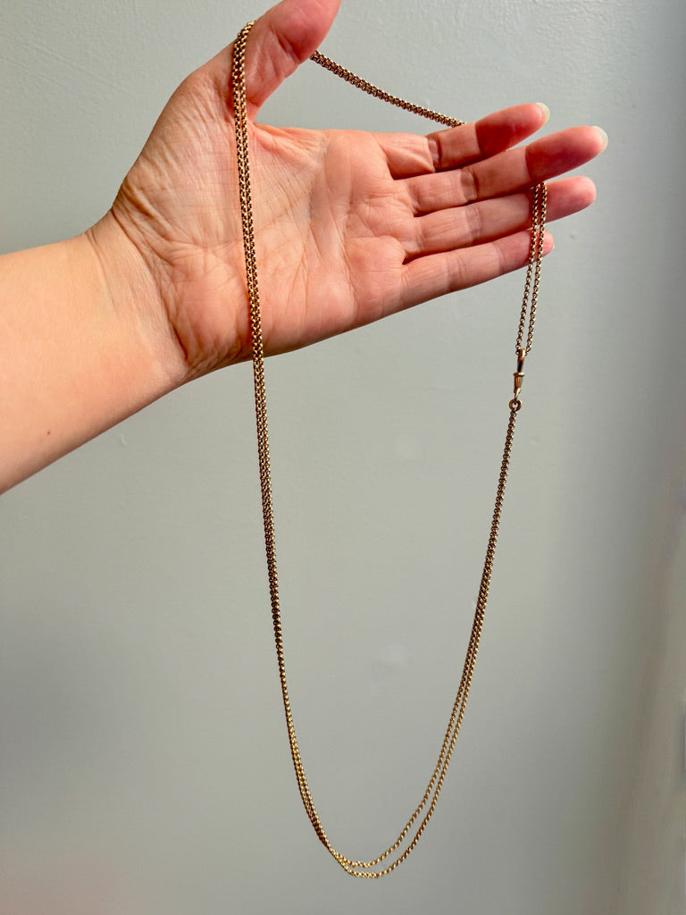 Gold chain held in a hand against a neutral background