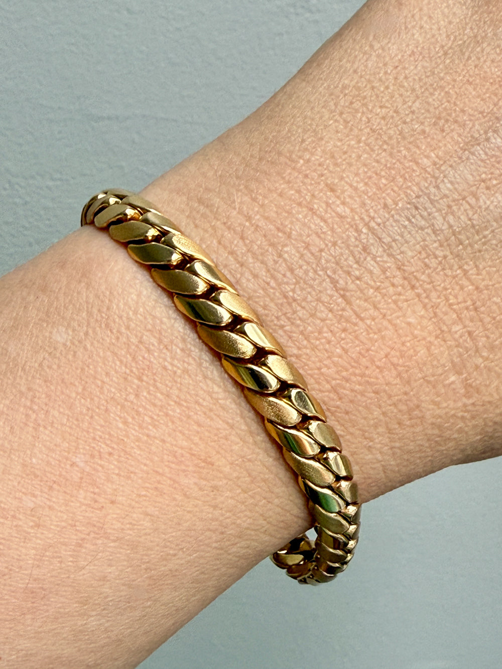 Gold chain bracelet on a wrist against a light gray background