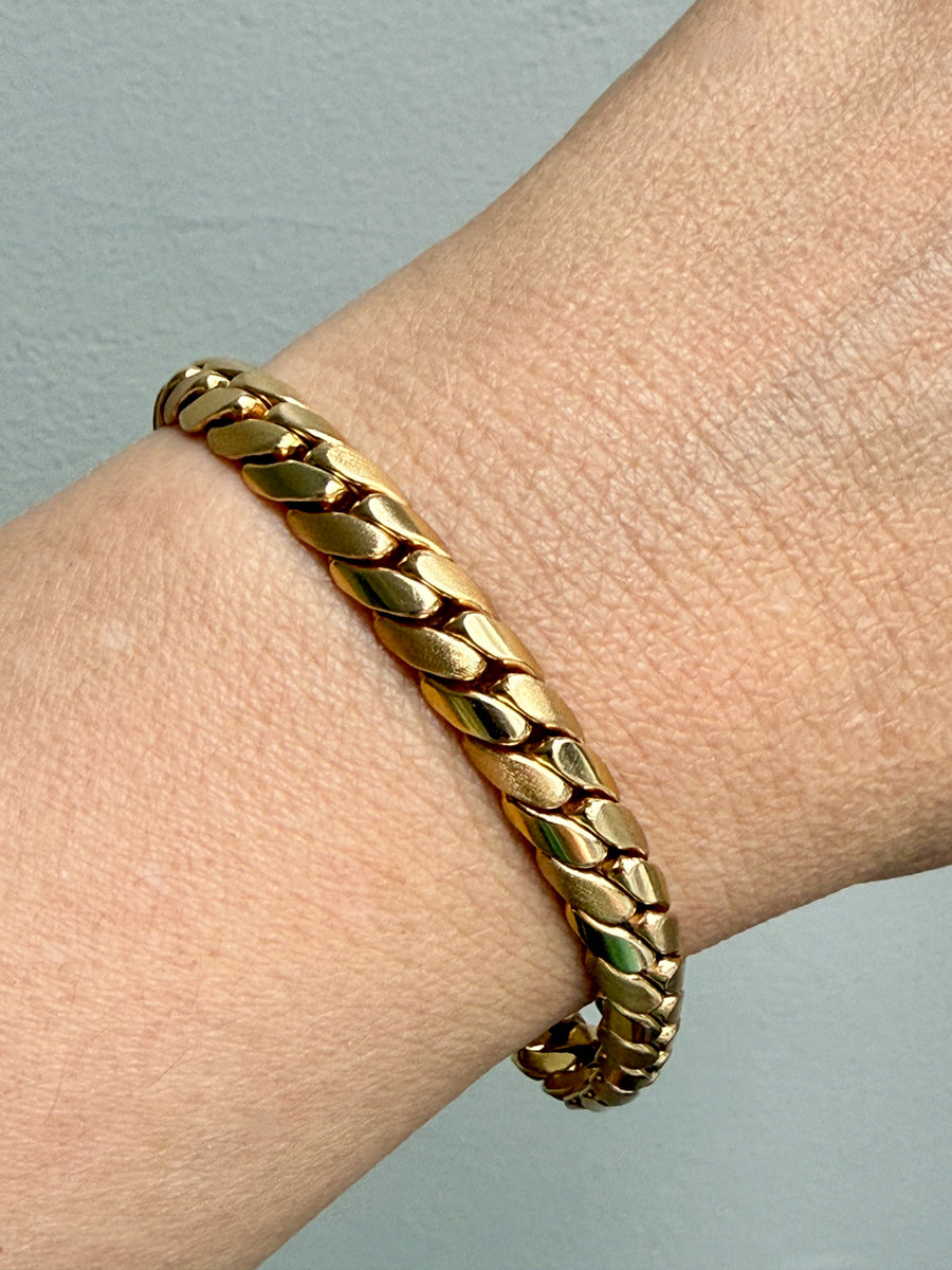 Gold chain bracelet on a wrist against a light gray background