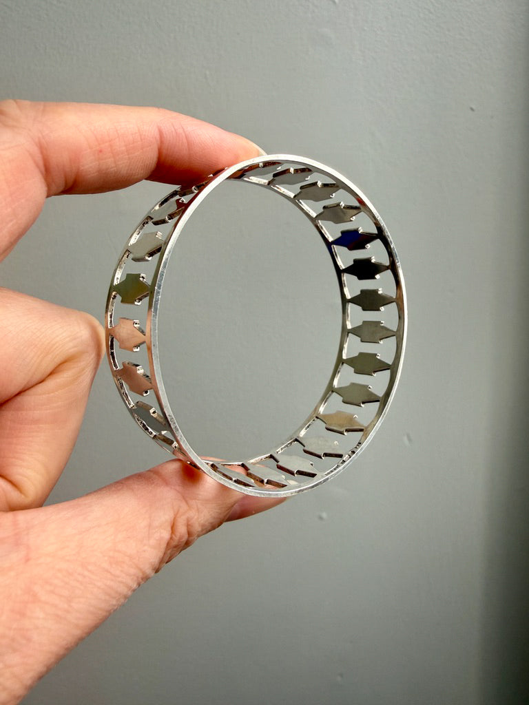 Hand holding a silver vintage bangle with geometric design against a gray background