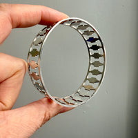 Hand holding a silver vintage bangle with geometric design against a gray background