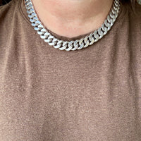 A close-up of a person wearing a chunky silver Cuban link chain necklace over a brown knit top.