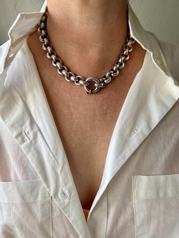 Person wearing a silver chain necklace with a white shirt.