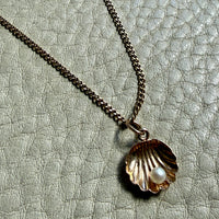 Necklace with a shell pendant and pearl on a textured gray background