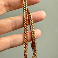 Gold chain held between fingers against a neutral background