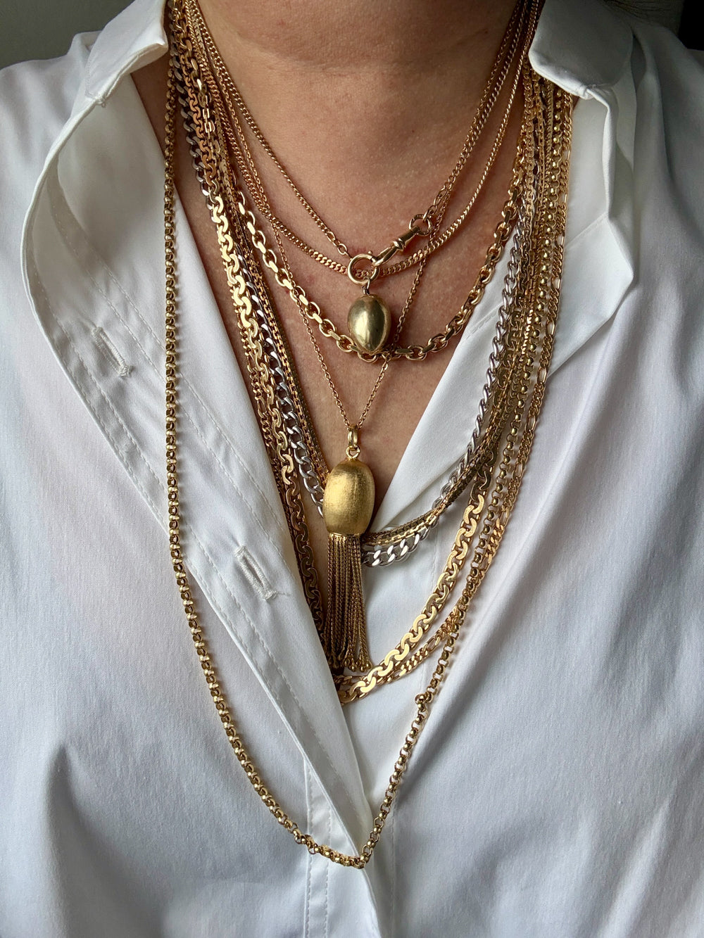 Person wearing multiple gold necklaces on a white shirt