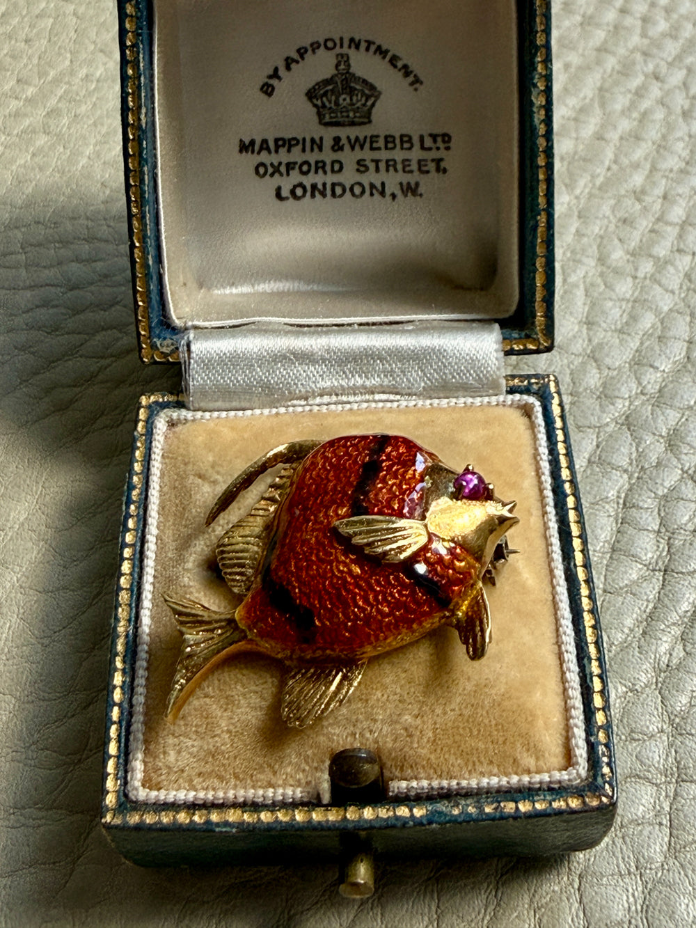 Gold fish brooch in an open jewelry box with Mappin & Webb branding.