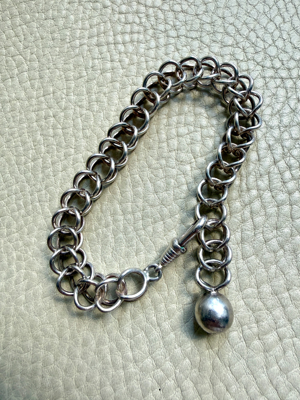 Silver chain bracelet with a pendant on a textured light gray background