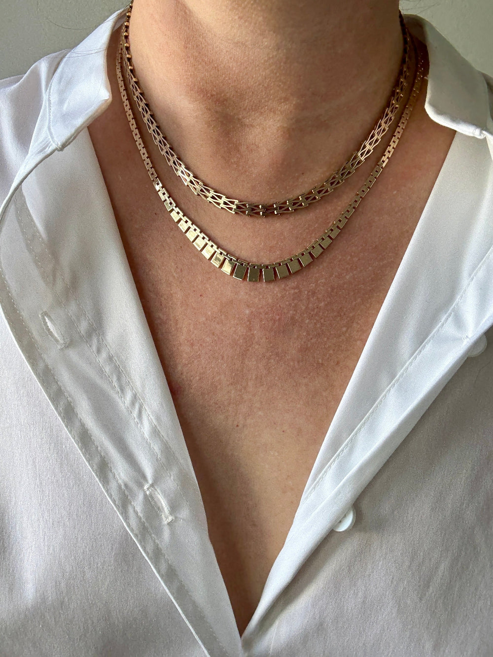 Close-up of a person wearing a white shirt with gold necklaces.