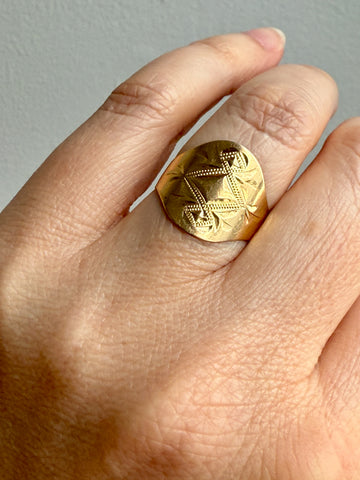Gold ring with intricate design on a finger against a neutral background
