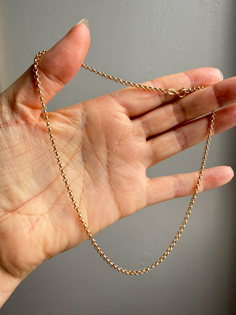 Gold chain held in a hand against a neutral background