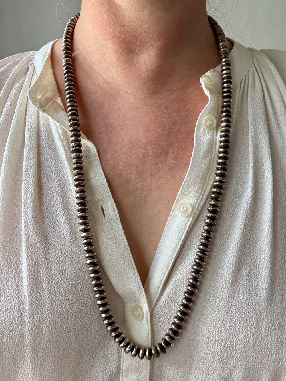 Person wearing a long silver beaded necklace with a plain background