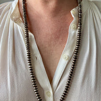 Person wearing a long silver beaded necklace with a plain background