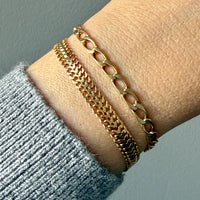 Two 18k gold vintage chain bracelets stacked on a person's wrist, with a gray knit sweater cuff visible at the lower left against a muted gray background.