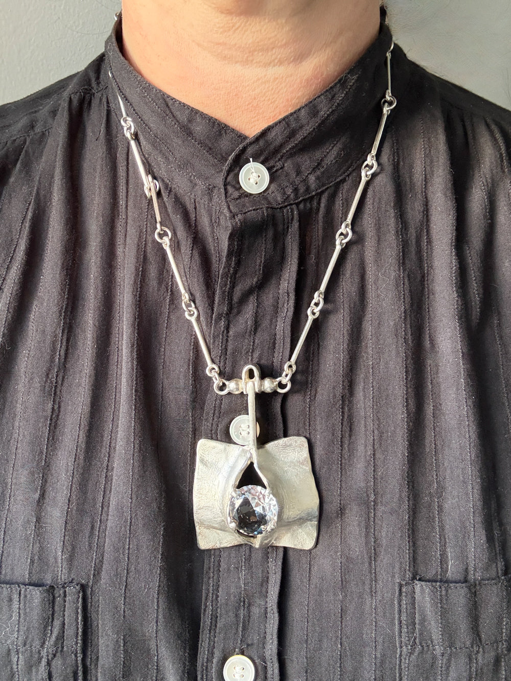 Person wearing a dark shirt with a necklace featuring a unique pendant.