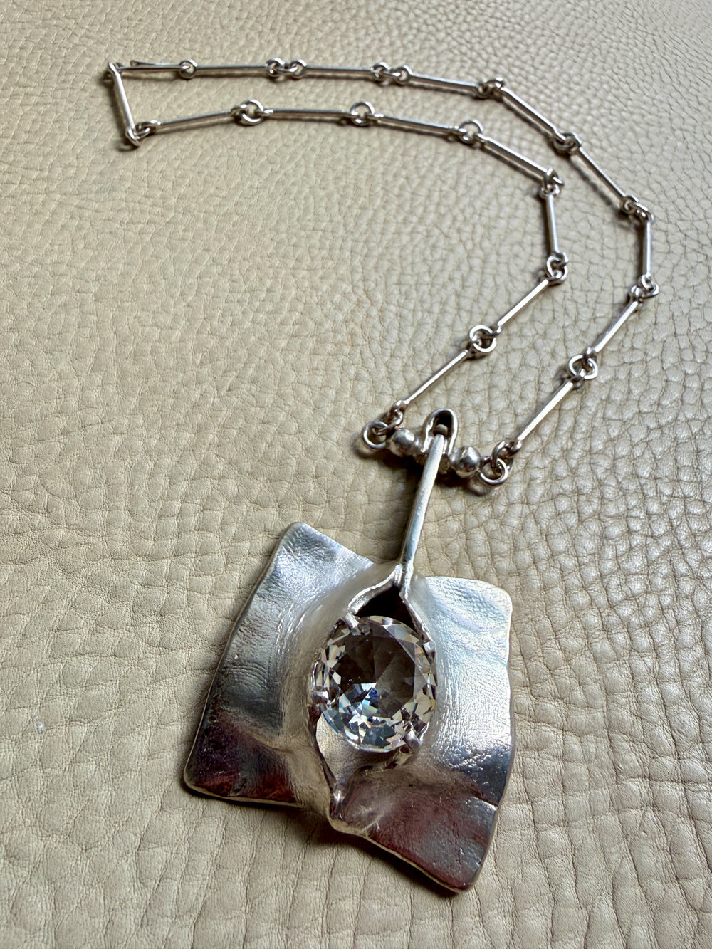 Silver necklace with a pendant on a textured beige surface