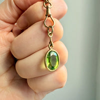 18k Gold pendant with a green peridot gemstone held in a hand against a neutral background