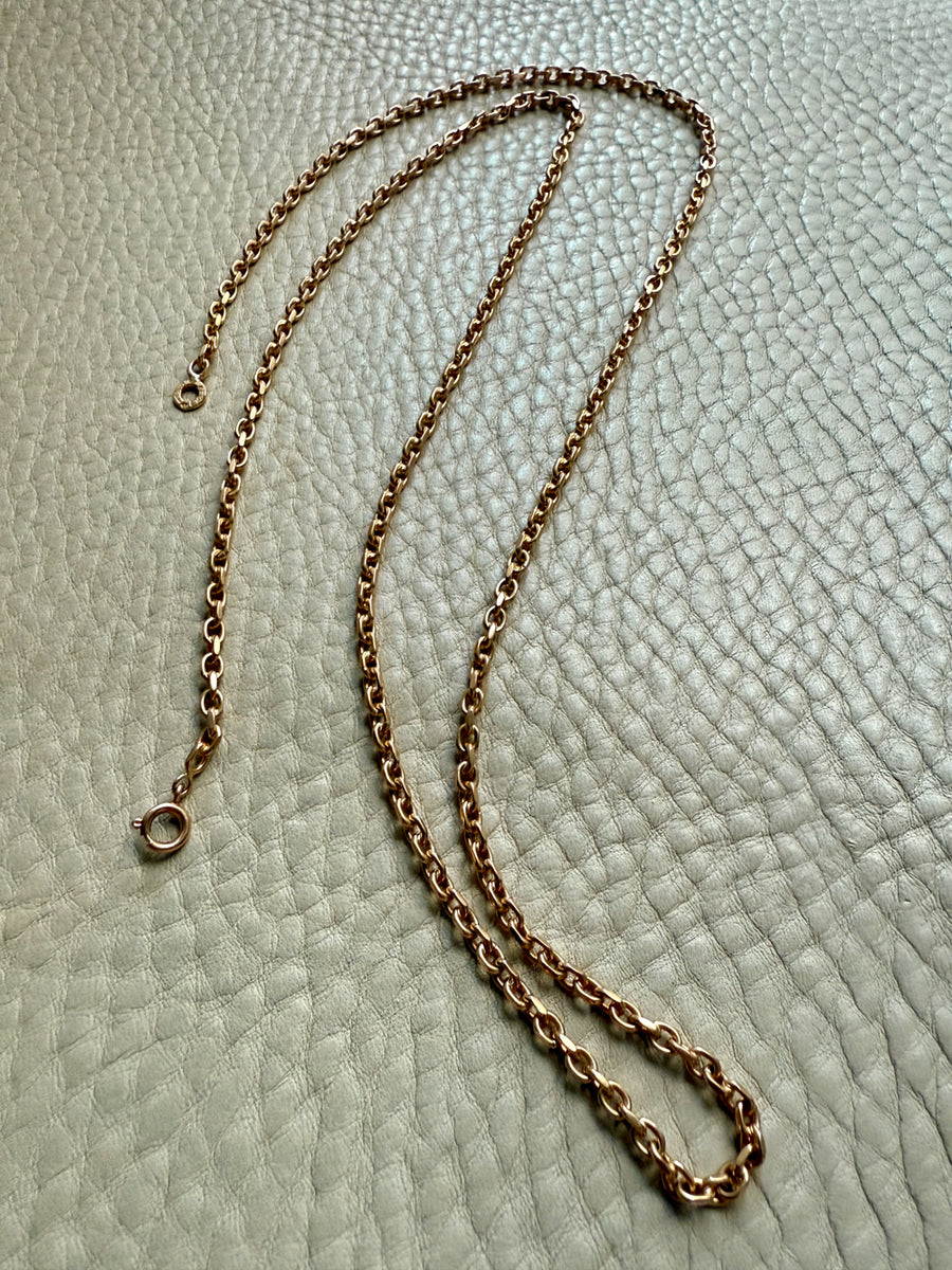antique gold chain necklace on a textured light gray background
