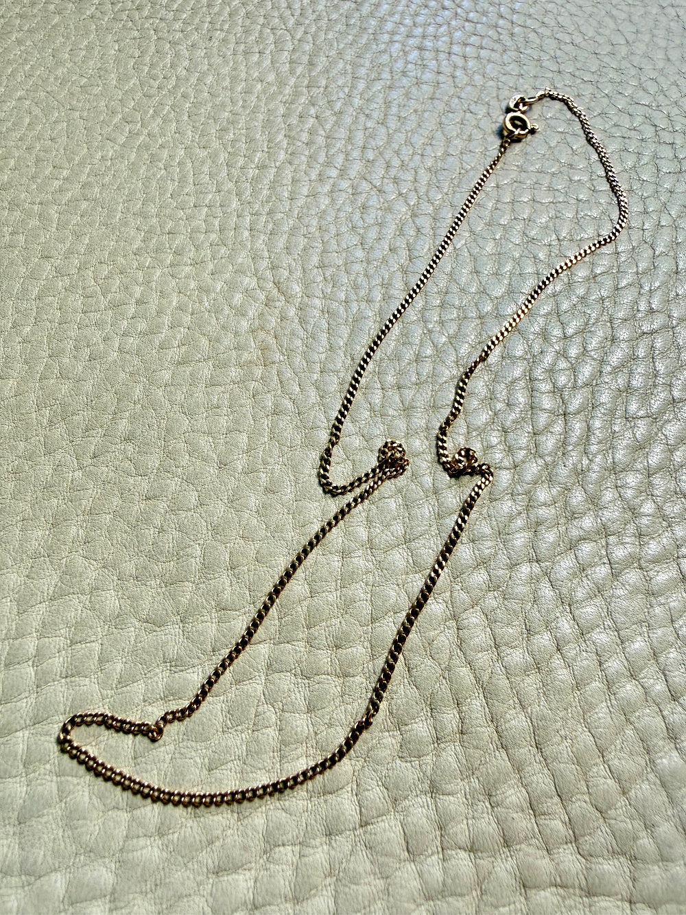 18k gold curb Necklace with a clasp on a textured light gray surface