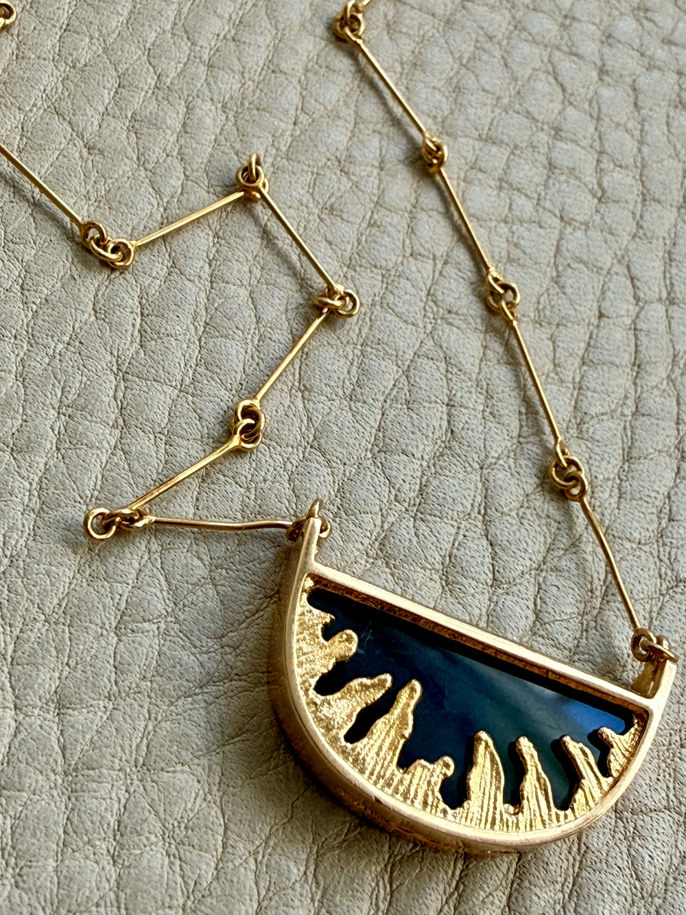 Gold necklace with a half-circle pendant on a textured beige background