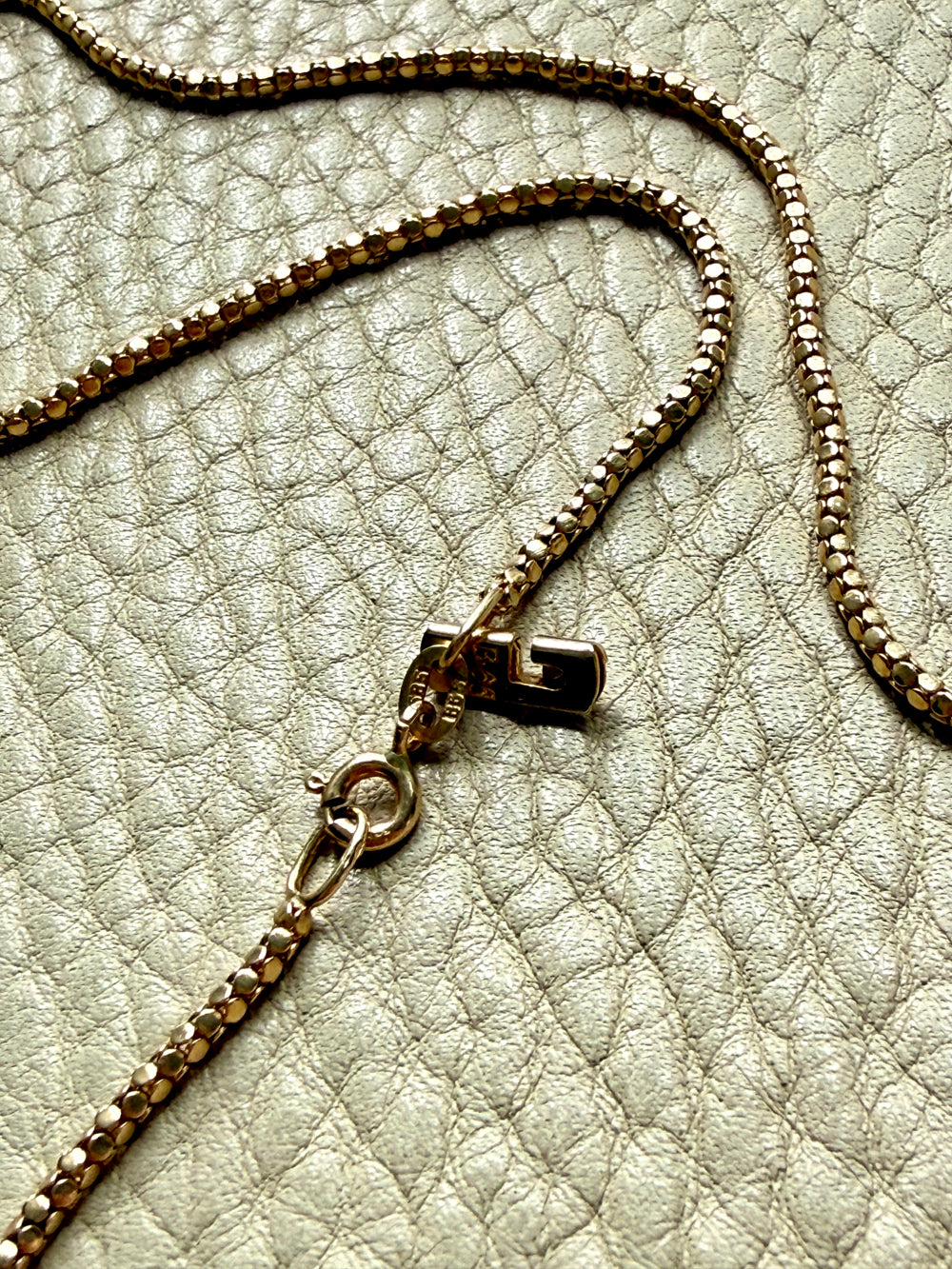 Close-up of a gold chain necklace on a textured beige surface
