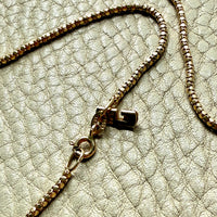 Close-up of a gold chain necklace on a textured beige surface