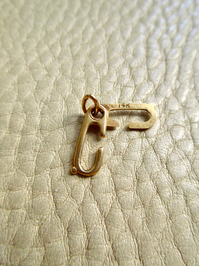 A small 14k gold sister clasp pendant holder, placed on a textured off-white leather surface. penelopepenelope.com