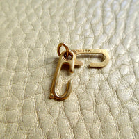 A small 14k gold sister clasp pendant holder, placed on a textured off-white leather surface. penelopepenelope.com