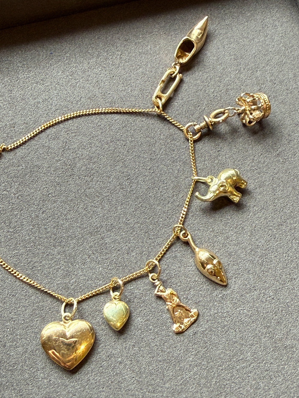 An 18k gold chain with multiple dangling animal and heart charms, laid flat on a textured gray surface. penelopepenelope.com
