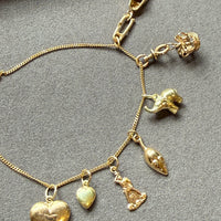 An 18k gold chain with multiple dangling animal and heart charms, laid flat on a textured gray surface. penelopepenelope.com