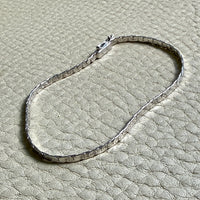 14k white gold bracelet on a textured beige surface