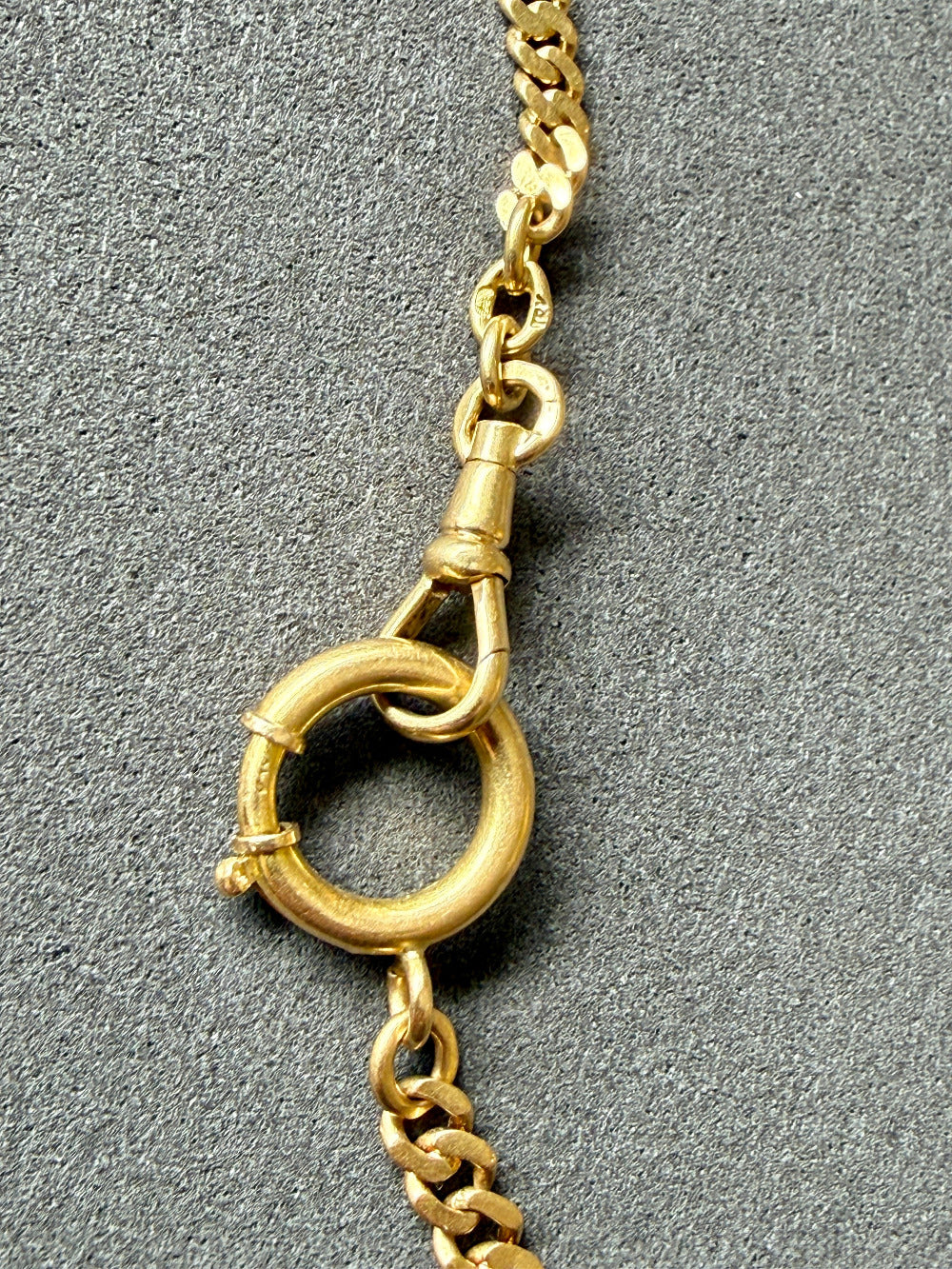 Close-up of a gold chain with a clasp on a gray background