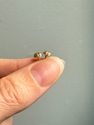 Gold earrings held between fingers against a neutral background