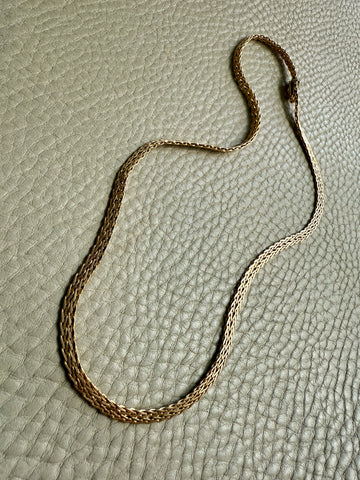 Gold chain necklace on a textured beige surface PenelopePenelope.com