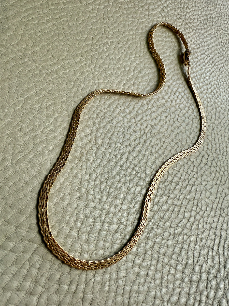 Gold chain necklace on a textured beige surface