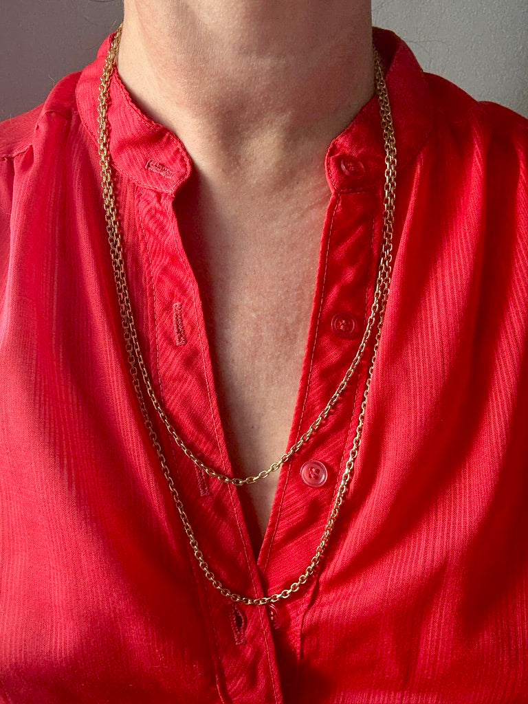 Red shirt with a gold chain necklace on a neutral background