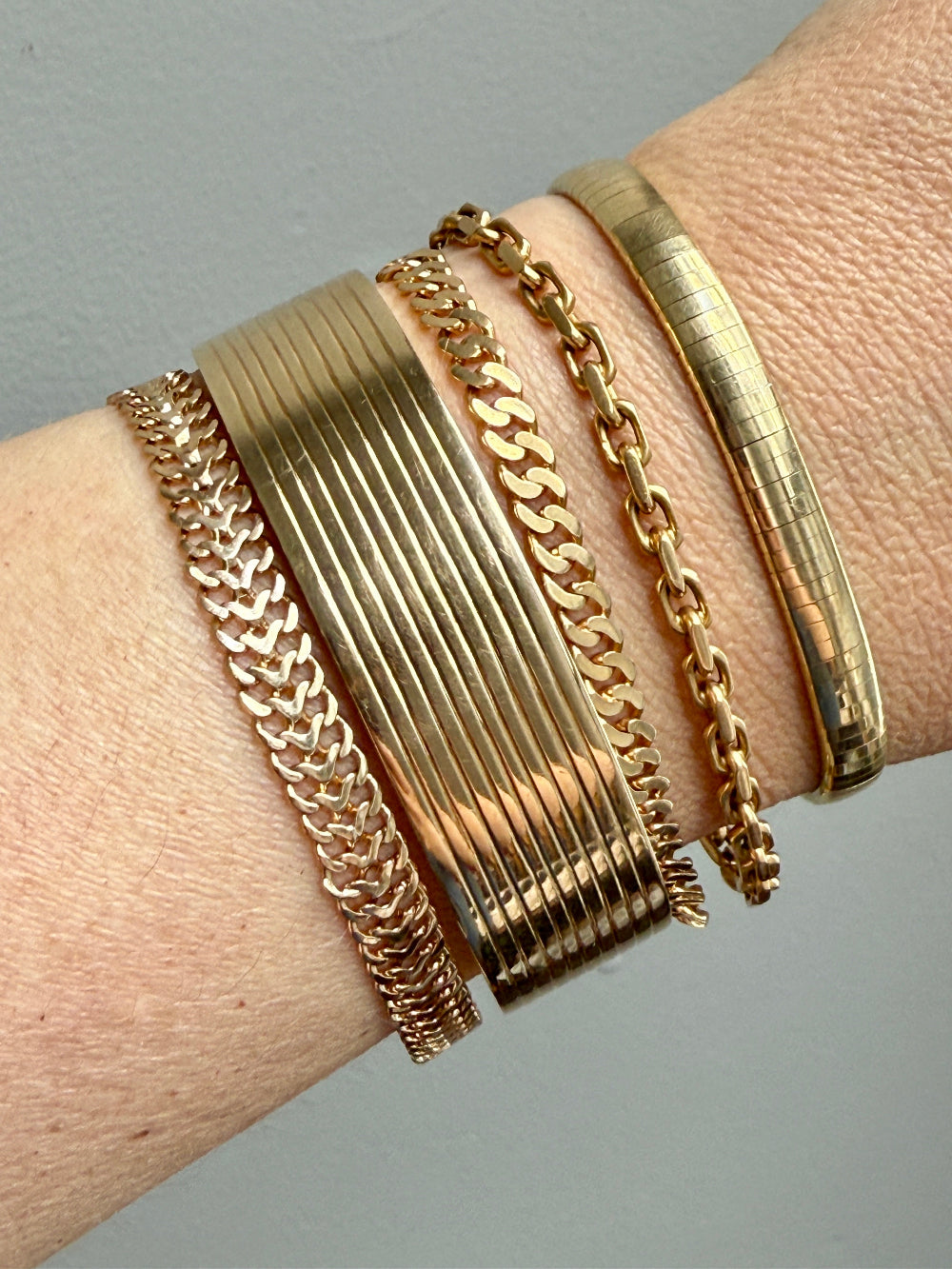 Gold bracelets on a wrist against a neutral background