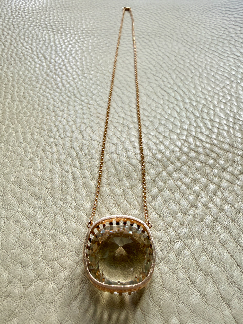 Gold necklace with a pendant on a textured beige surface