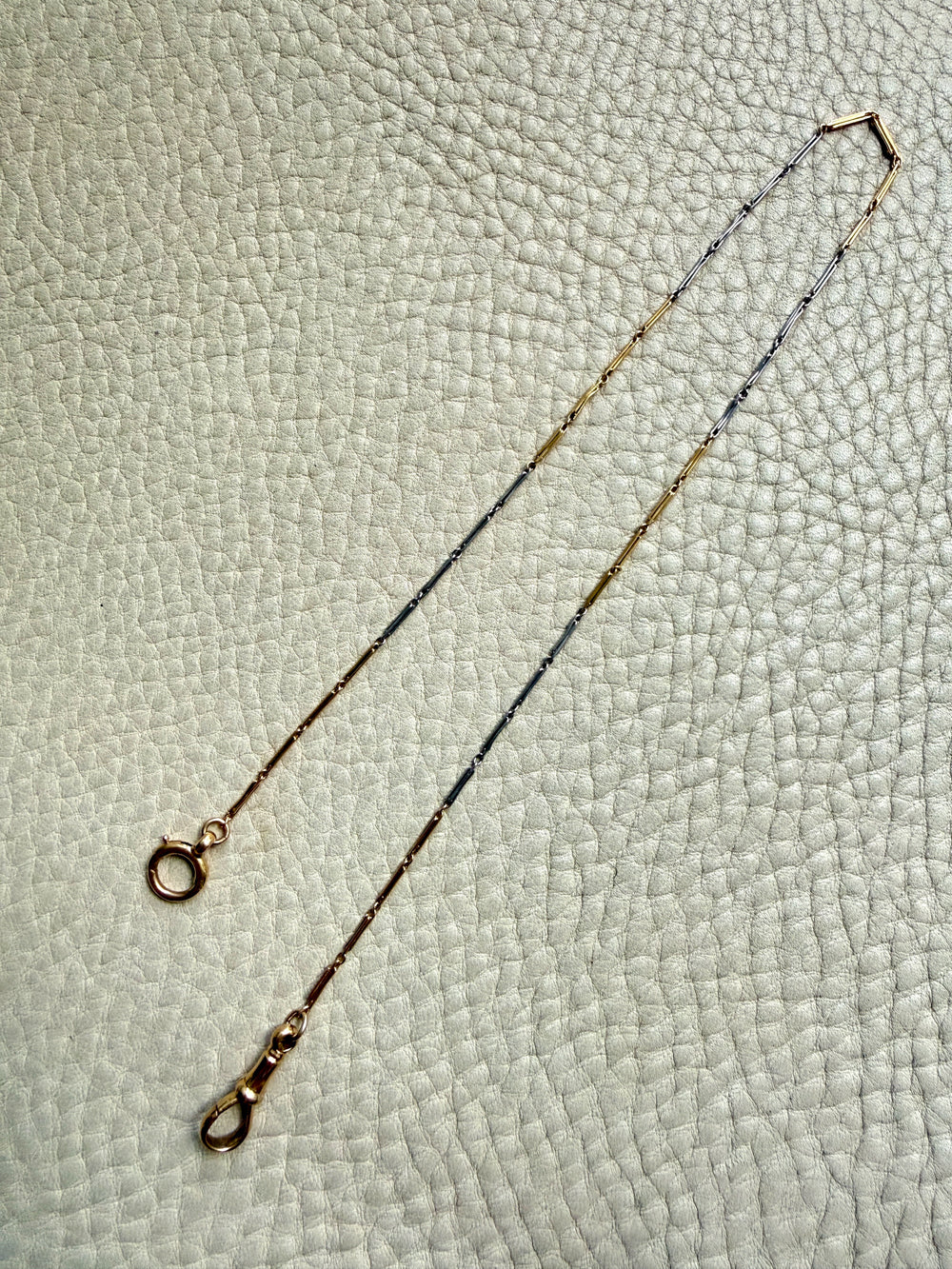 18k Gold and platinum watch chain with clip on a textured beige background