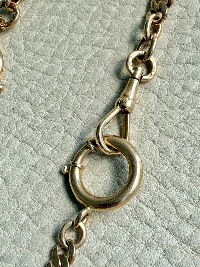 Close-up of a gold chain with a clasp on a textured light gray background