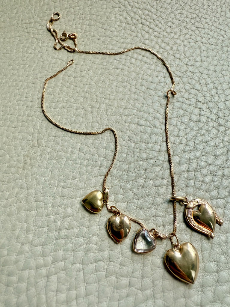 Gold necklace with heart-shaped pendants on a textured light gray surface