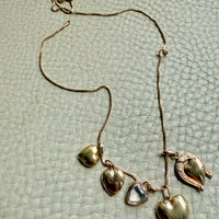 Gold necklace with heart-shaped pendants on a textured light gray surface