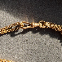 Close-up of a gold chain with a dog clip on a textured gray surface