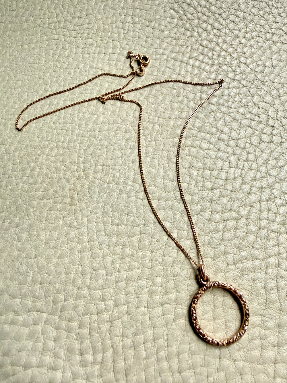 18k gold necklace with a circular pendant on a textured light green surface