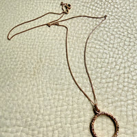 18k gold necklace with a circular pendant on a textured light green surface