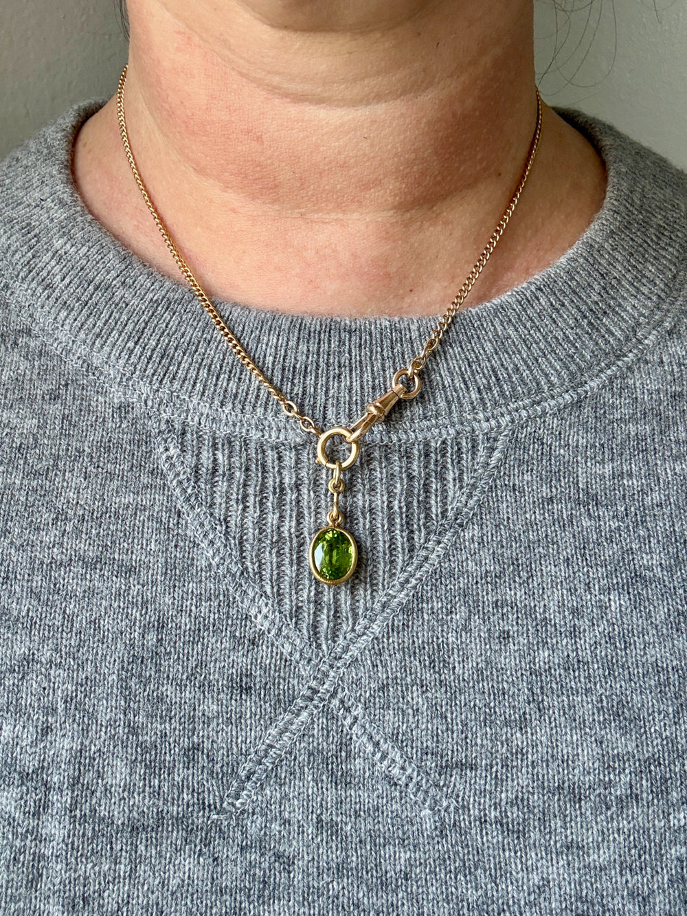 Necklace with a green pendant worn by a person in a gray sweater.