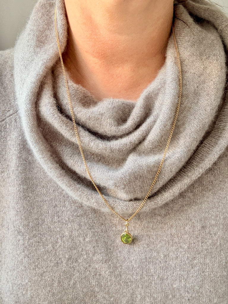 Necklace with a green pendant worn by a person in a gray sweater.
