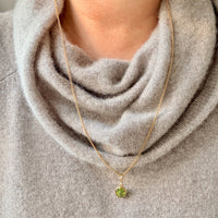 Necklace with a green pendant worn by a person in a gray sweater.