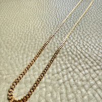 Gold chain necklace on a textured beige surface