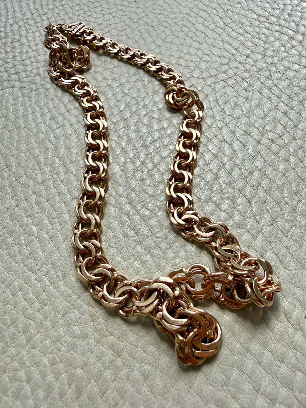 A chunky rose gold chain necklace displayed on a textured off-white surface.